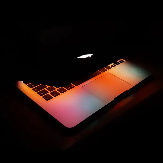 an apple laptop lit up in the dark